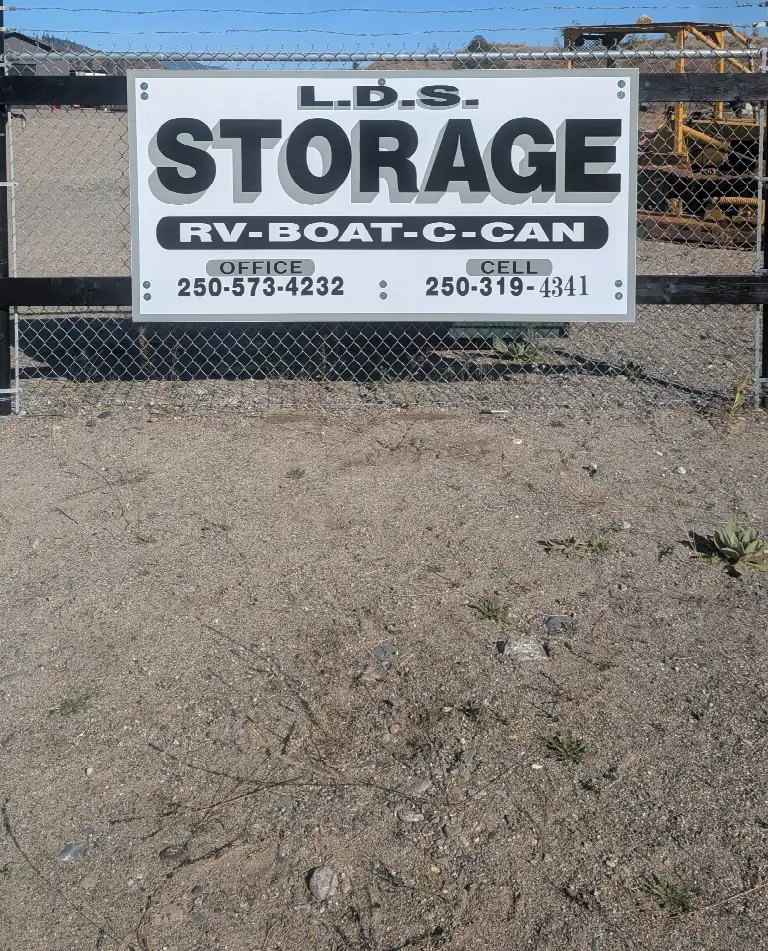 The L.D.S. Storage sign on the yard fence: RV, boat and C-can storage, with office and cell numbers