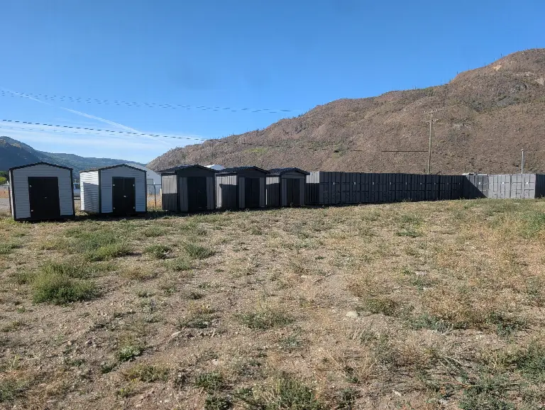 A row of storage sheds beside a long wall of charcoal sea cans at the L.D.S. Storage yard, below the hills